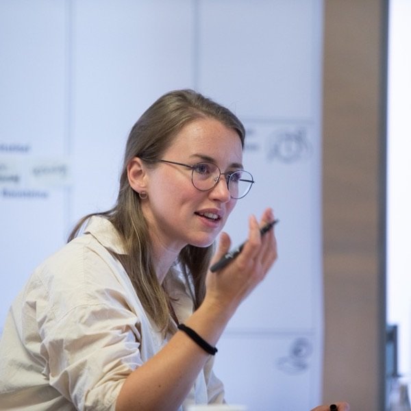 Lia Weitz in conversation during a workshop, an annotated board behind her