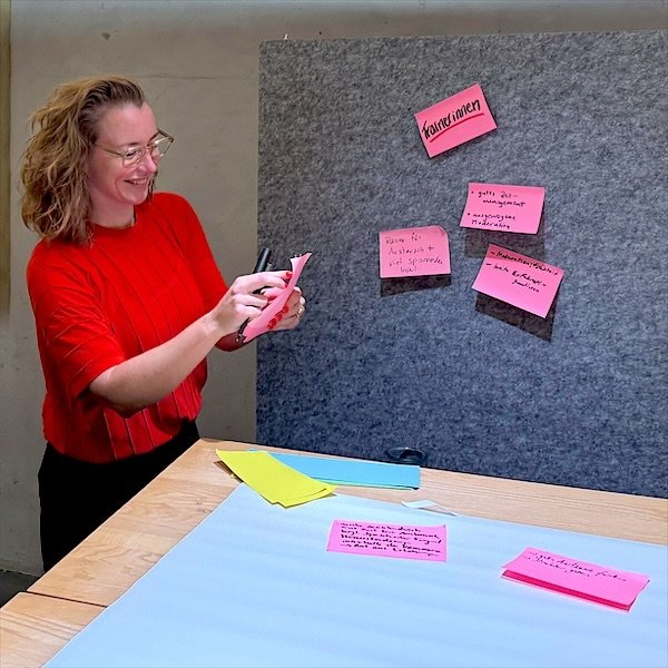 Lia Weitz souriant en regroupant des cartes de facilitation devant un panneau d’affichage