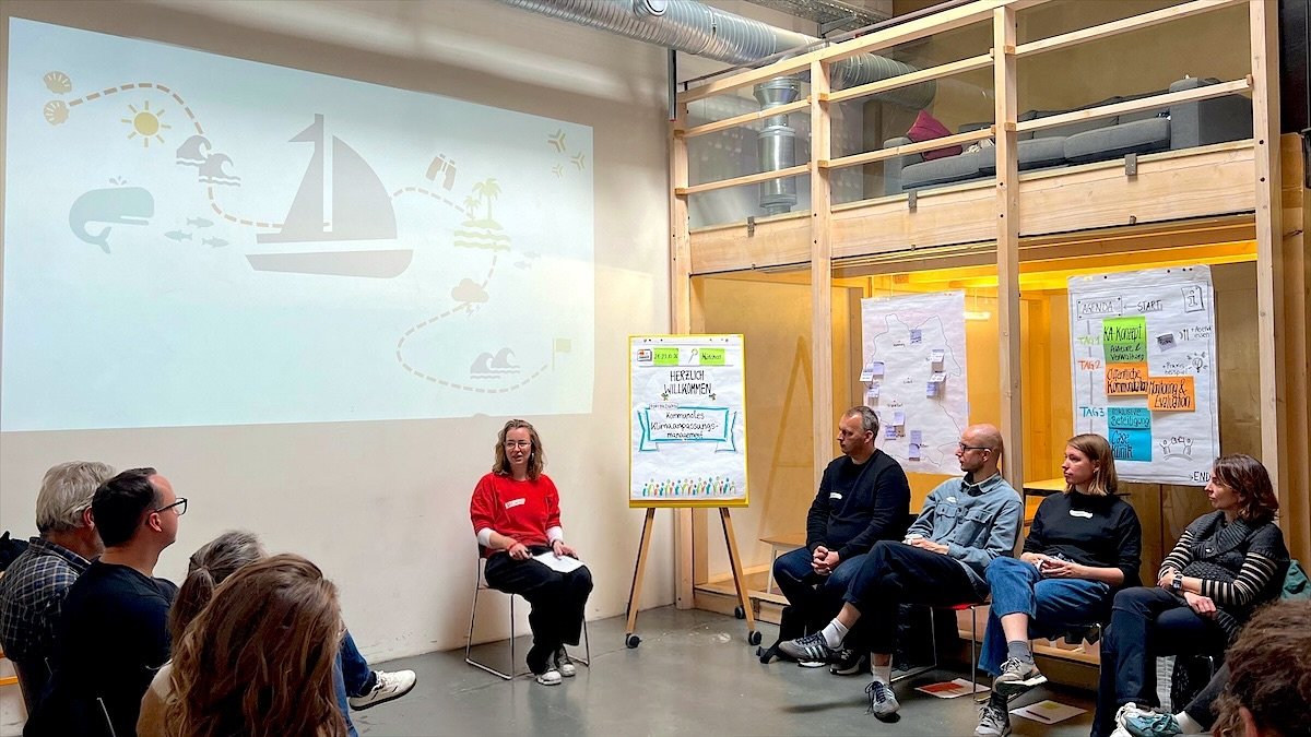 Lia Weitz en cercle avec les participant·es d’une formation sur l’adaptation municipale au changement climatique, entourée de paperboards illustrés